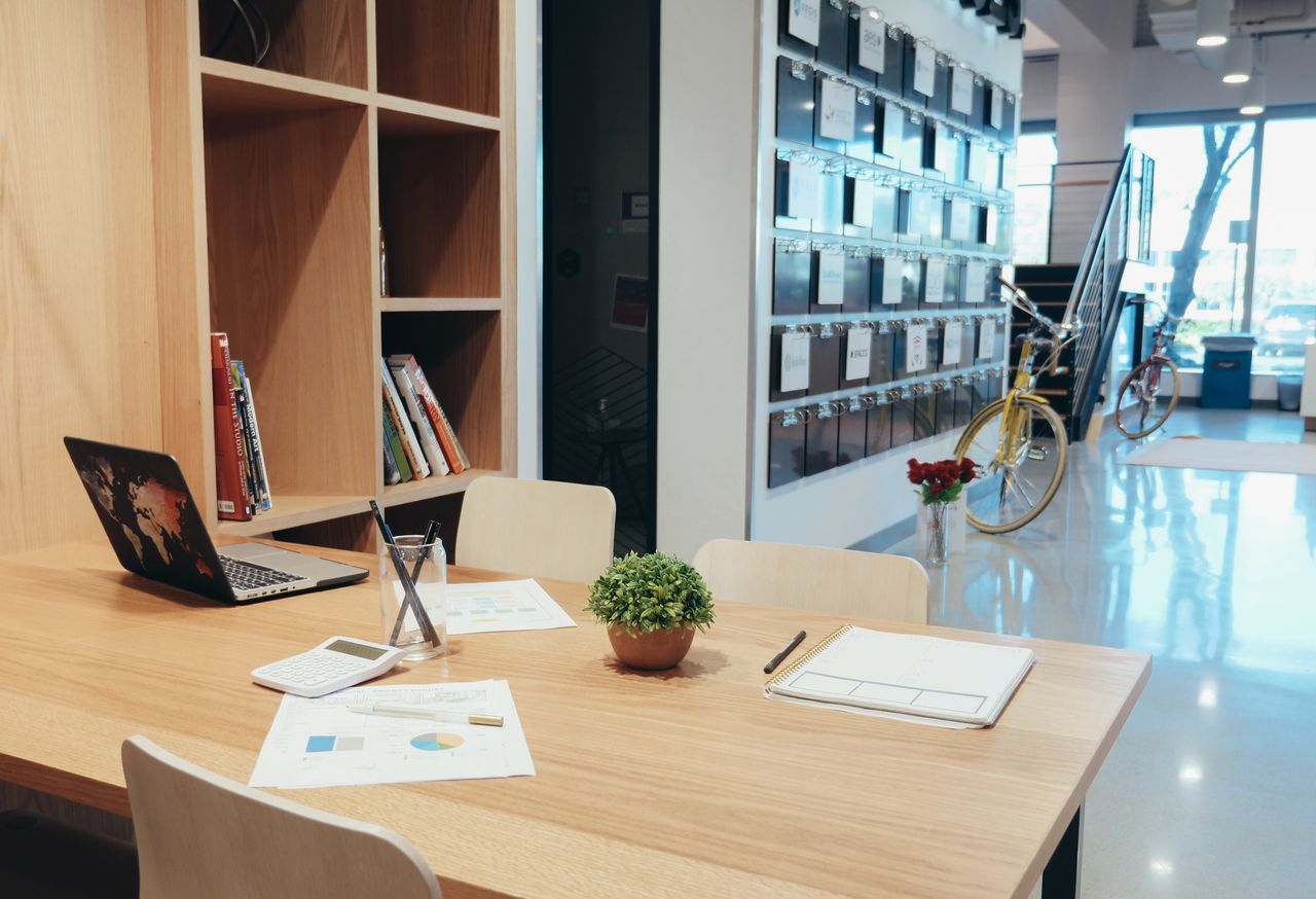 A modern office workspace featuring a laptop, documents, and a potted plant on a wooden table.
